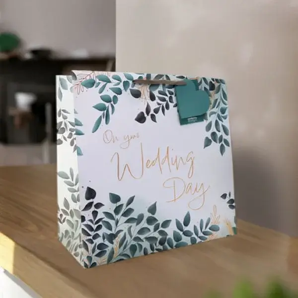 A wedding gift bag decorated with leafy foliage and gold lettering reading On your Wedding Day, displayed on a wooden surface.